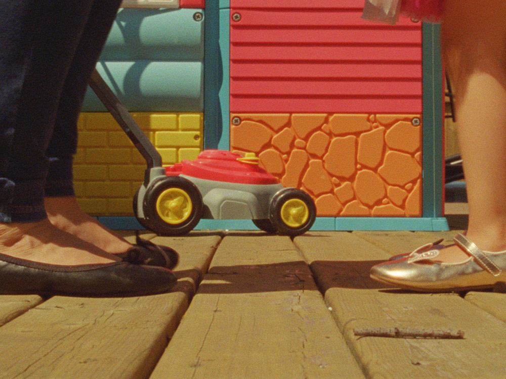 Mother and daughter's feet set against play house and plastic lawnmower