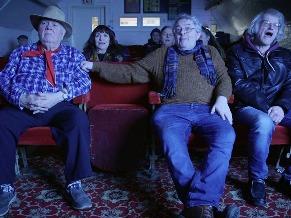 A group of people laugh at a cinema screen in a small community cinema