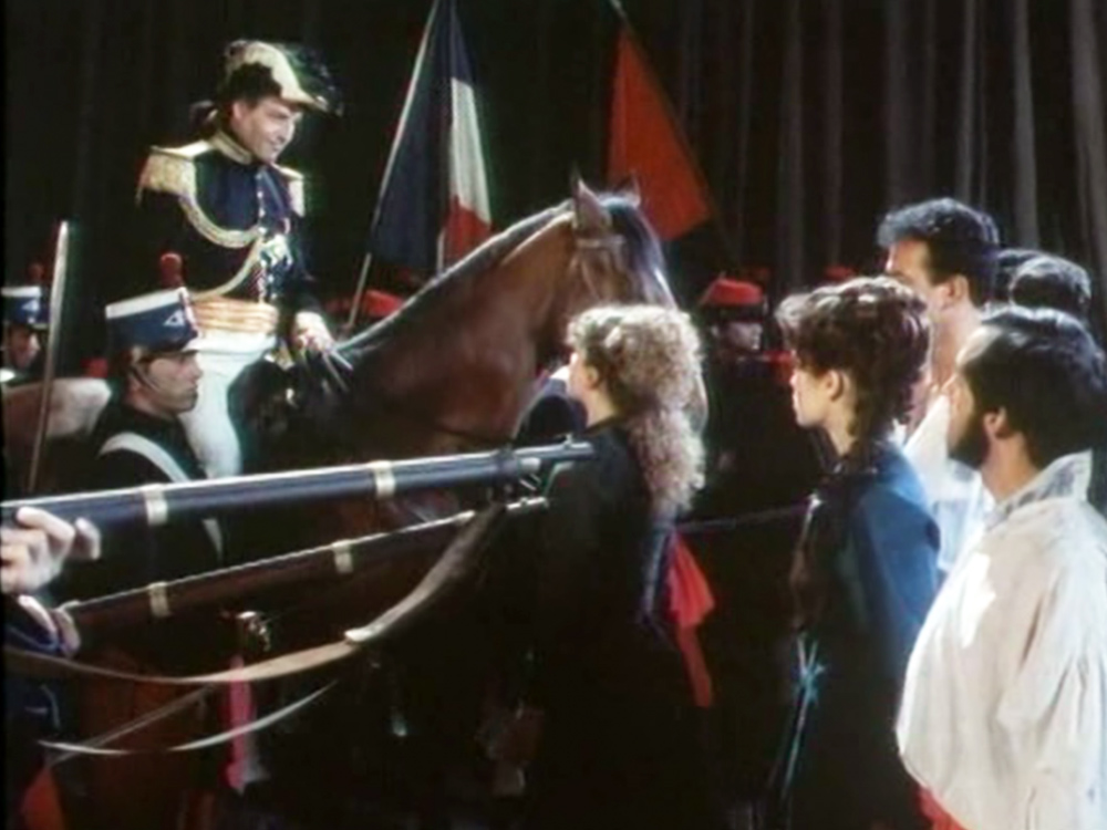 A French soldier on a horse looks down at people gathering in front of his horse. A gun points through half the image